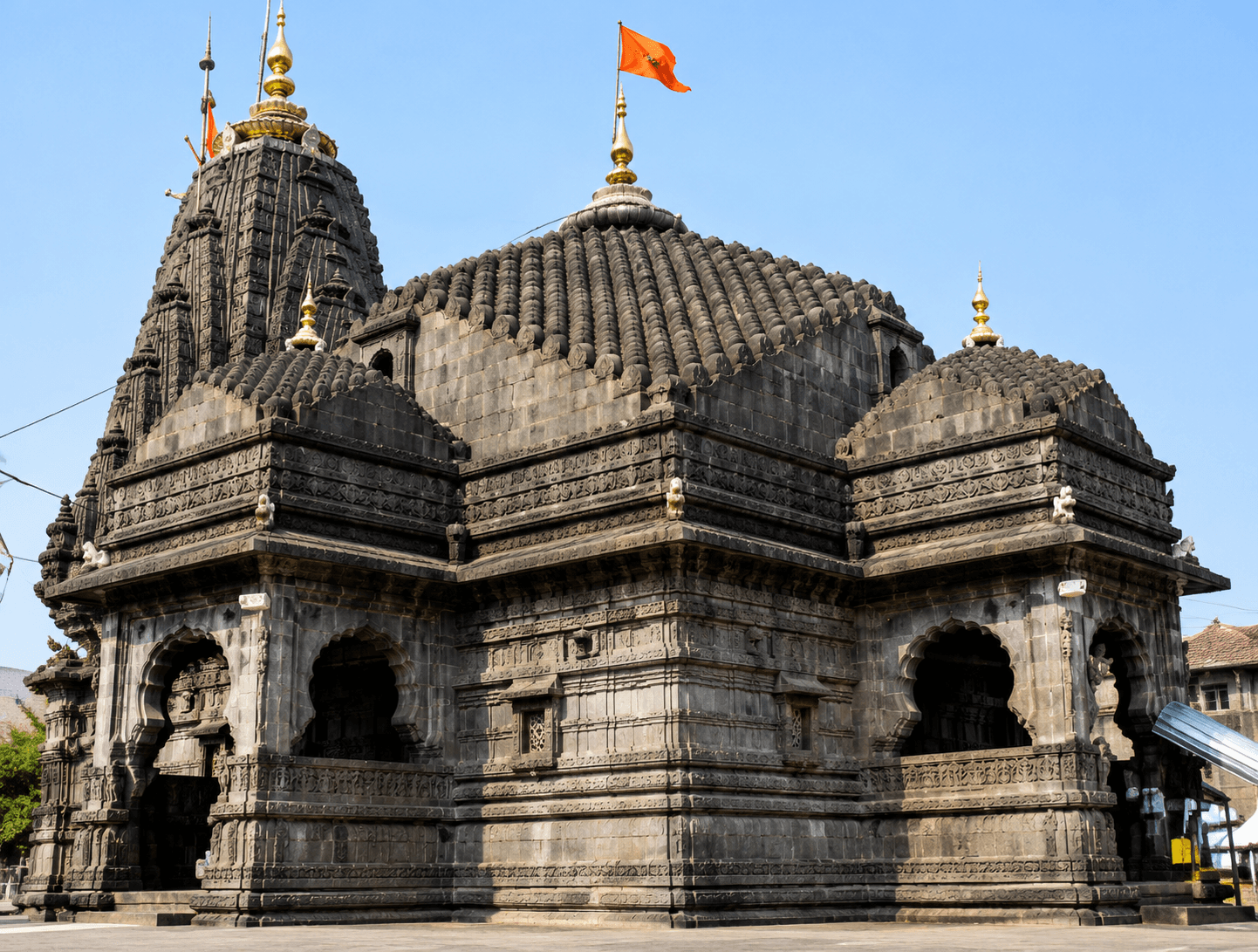 Trimbakeshwar Temple's carved basalt shikhara and saffron flag against a clear blue sky